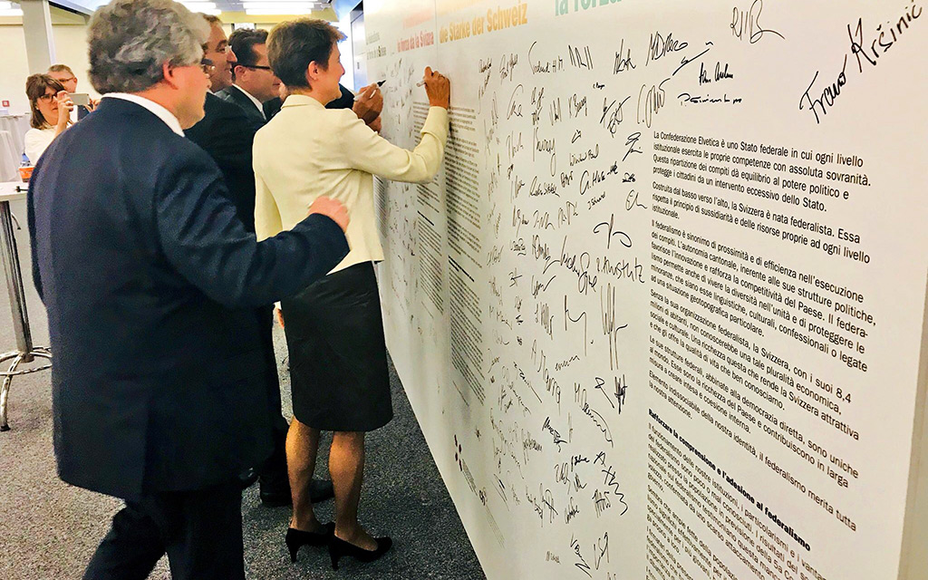 Bundesrätin Simonetta Sommaruga steht vor einer Wand und unterzeichnet die dort aufgedruckte Erklärung von Montreux